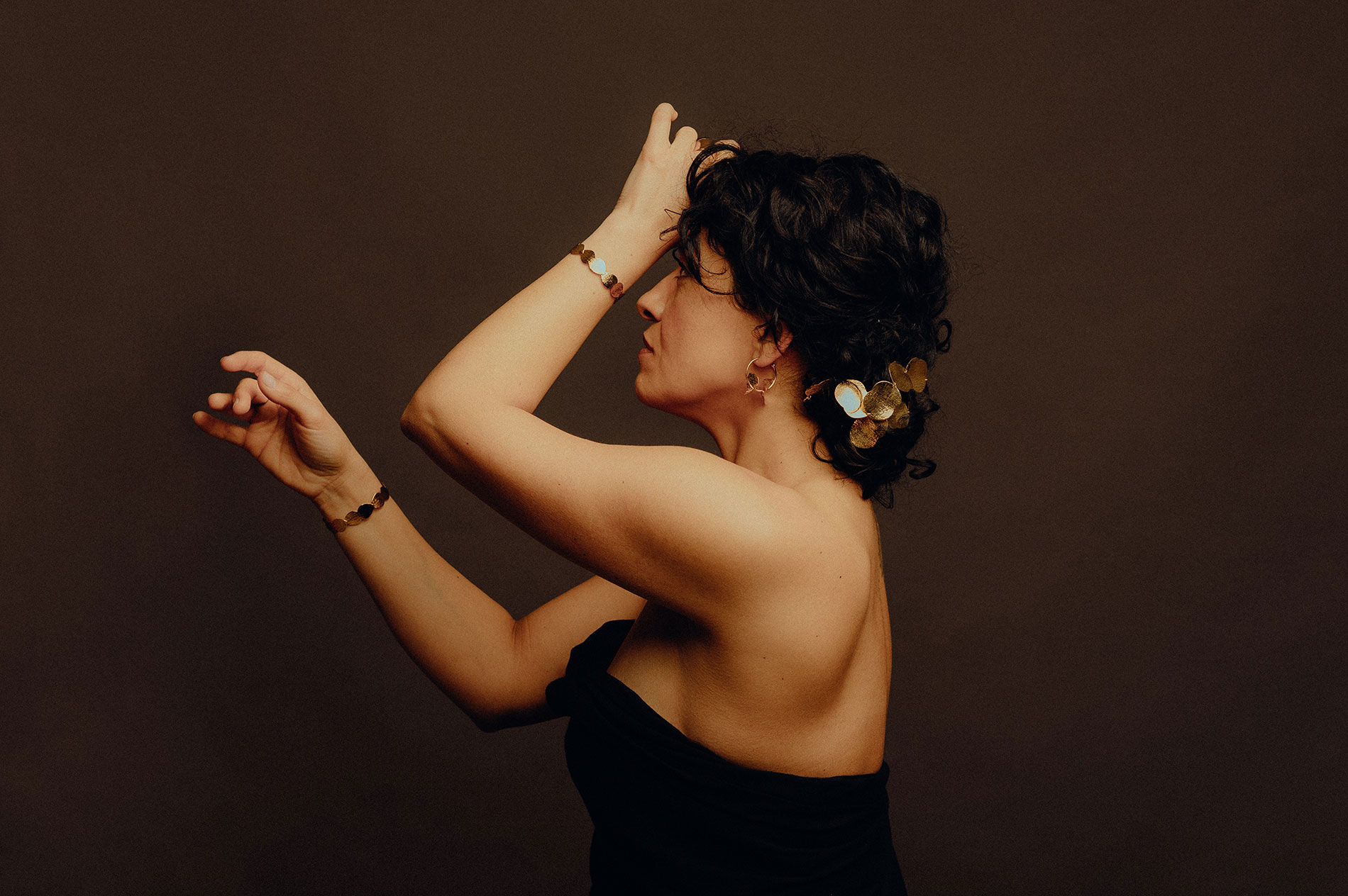 Femme de profil, bras levés, portant la parure Carpe Diem en laiton doré : bracelets, boucles d'oreilles et ornement de cheveux feuillage, Les Aubépines
