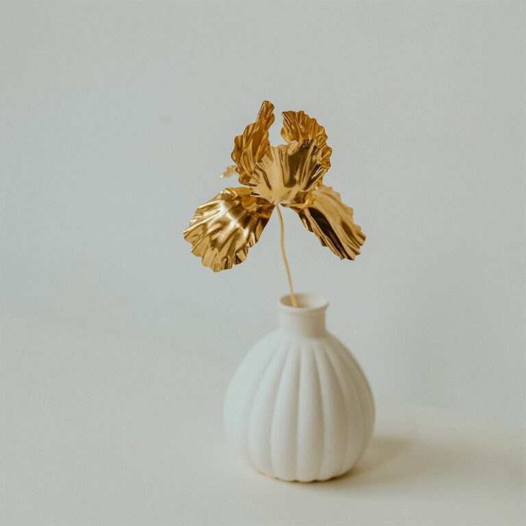 sculpture fleur d'iris en laiton doré déposée dans un vase en porcelaine blanche pour sublimer un espace. Fabriquée par l'artiste Agnès Nicot à Limoges
