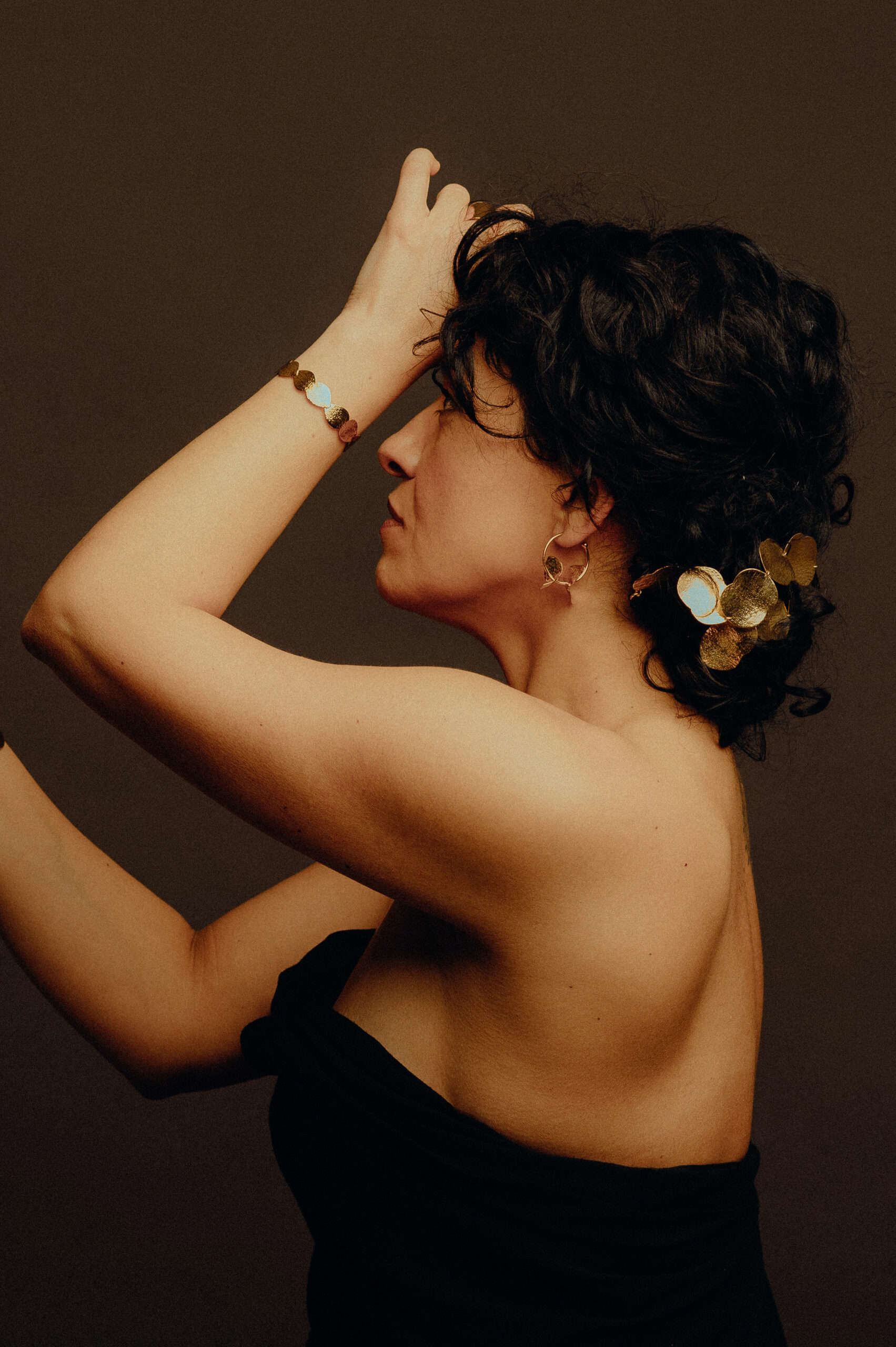 Femme de profil, bras levés, portant la parure Carpe Diem en laiton doré : bracelets, boucles d'oreilles et ornement de cheveux feuillage, Les Aubépines