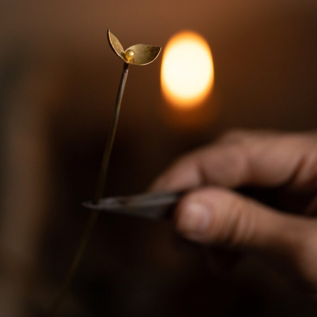 Jeune pousse en laiton tenue à la pince devant la flamme d'une bougie, dans l'atelier Les Aubépines