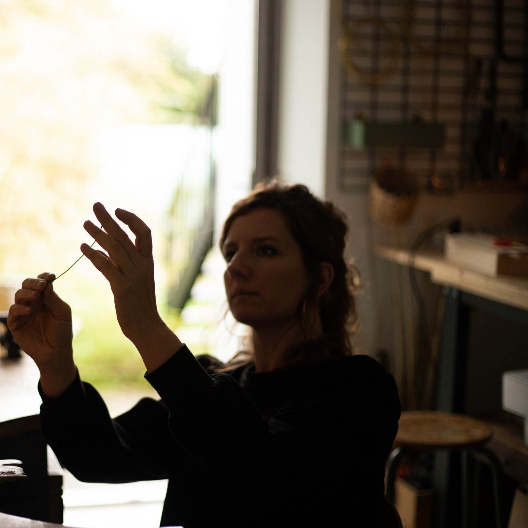 Agnès Nicot en contre-jour dans son atelier, observant un fil de laiton